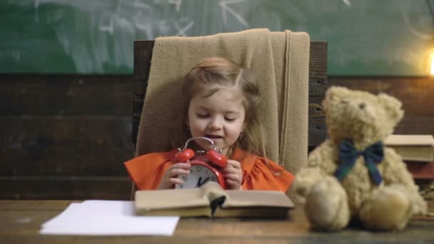 유치원 교실에서푸 틸을 귀엽게 먹어요. 책상에 앉아서 자명종 시계로 놀고 있는 어린 소녀. 아이들 교육, 홈 스쿨링. 수업중인 귀여운 여대생. — 비디오
