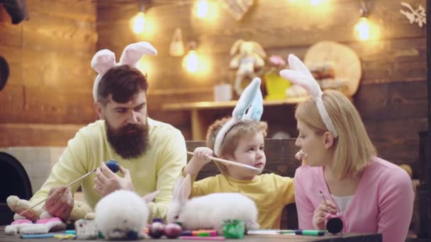 Щаслива сім'я малює яйця на Великодні канікули. Мати, батько і син дитина в вухах кролика . — стокове відео