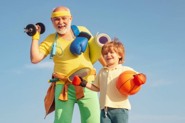 Aile sporu. Büyükbabam ve torunum ellerinde basketbol topu ve yoga minderiyle. Aile sağlık kulübünde kıdemli adam ve çocuk..