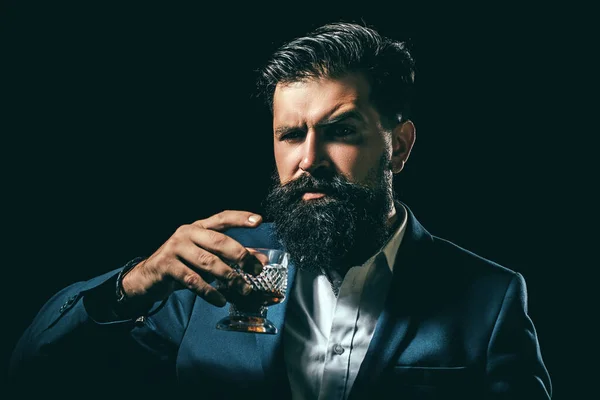 Barbudo y vaso de whisky. Hombre camarero con barba sostiene brandy de vidrio. Concepto de alcohol. Elegante hombre barbudo elegante camarero sostiene vaso de whisky. — Foto de Stock