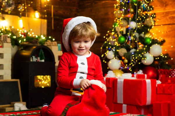 Schöne Baby genießen Sie Weihnachten. Kind an Christbaum und Kamin an Heiligabend. Familie mit Kindern feiert Weihnachten zu Hause. Kleiner Junge schmückt Weihnachtsbaum und öffnet Geschenke. — Stockfoto