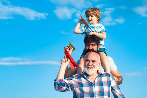Множество поколений. Семейный уикенд. Мужчины разного возраста. Счастливый ребенок играет с игрушечным бумажным самолетом на фоне летнего неба. Ребенок счастлив. Отец и сын играют на голубом летнем небе. — стоковое фото