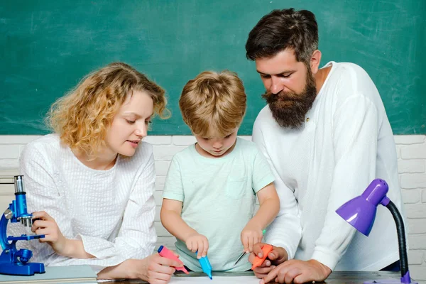 Partnerschaftsmodelle für Schulgemeinschaften. Grundschüler. Glückliches junges Paar, das mit seinem Sohn beim Abschluss steht. Junges Paar hilft seinem Sohn bei den Hausaufgaben. — Stockfoto