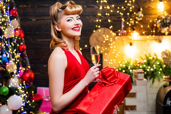 Modieus luxe meisje dat nieuwjaar viert. Retro vrouw bij de kerstboom. Glimlachende vrouw in de avond rode jurk met glas mousserende wijn over huis Kerstboom achtergrond. — Stockfoto