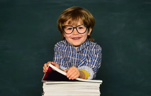 Χαριτωμένο αγόρι με χαρούμενη έκφραση προσώπου κοντά στο γραφείο με σχολικά είδη. Πρώτη μέρα στο σχολείο. Μαθαίνεις από σχολιαρόπαιδο ή από νηπιαγωγείο. Προσχολικός — Φωτογραφία Αρχείου