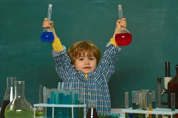Skolbegreppet. Utbildning. Glada leende liten pojke som har kul mot blå vägg. De utförde ett nytt kemiexperiment. Förskollärare. Barn i klassrummet med svarta tavlan på bakgrunden — Stockfoto