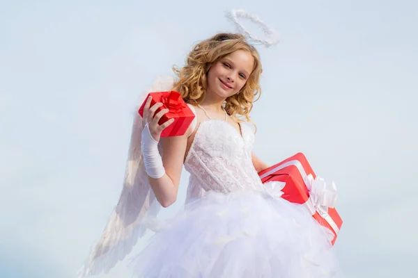 Niña pequeña con traje de ángel vestido blanco y alas de plumas. Lindo angelito Cupido con regalo. Tarjeta de felicitación de arte festivo. — Foto de Stock