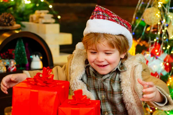 Emociones de regalo. Chico divirtiéndose cerca del árbol de Navidad en el interior. Chico gracioso sosteniendo regalo de Navidad. Lindos niños celebrando la Navidad. Niño de invierno. Concepto de año nuevo. — Foto de Stock