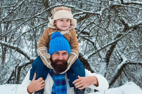 Father giving son ride on back in park. Child sits on the shoulders of his father. Christmas holidays and winter new year with father and son.