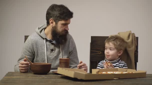 Ojciec i syn jedzą pizzę w domu. Chłopiec z ulubionym jedzeniem. Dzieci jedzenie koncepcja, szczęśliwy głodny człowiek jeść pizzę. — Wideo stockowe