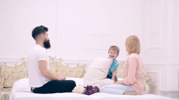 Boldog család, akik az ágyon játszanak és párnákat dobálnak. Apa, anya és fia ugranak párnákkal az ágyon.. — Stock videók