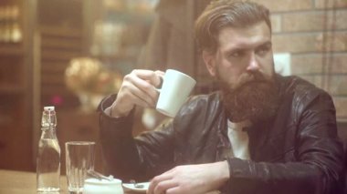 Genç sakallı adam kafede oturuyor. Birini beklerken kahve içen adam..