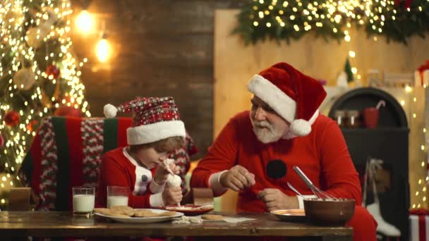 O avô a fazer bolachas de Natal com grangchild. Papai Noel assa pão de gengibre para criança em sua cozinha antes da véspera de Natal. — Vídeo de Stock