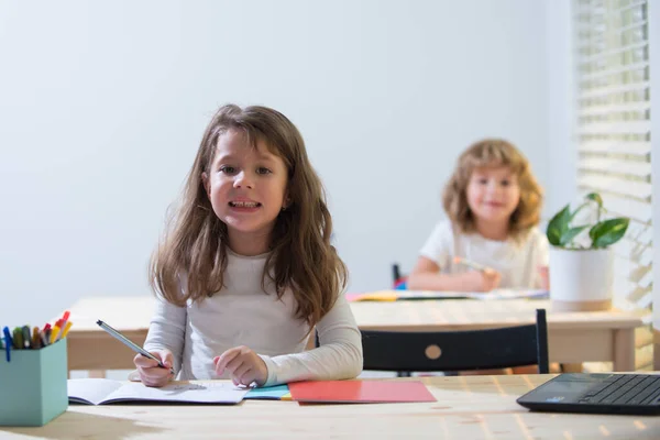 Graciosos niños sonrientes en clase en la escuela. Colegial y colegiala sentados en el escritorio y escribiendo un texto. — Foto de Stock