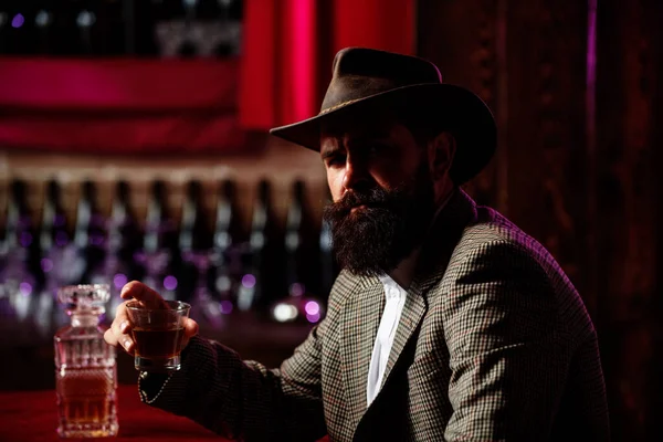 Portret brodatego mężczyzny z brodą. Macho pije. Stylowy bogacz trzymający szklankę starej whisky. Dżentelmen pije koniak lub whiskey. — Zdjęcie stockowe