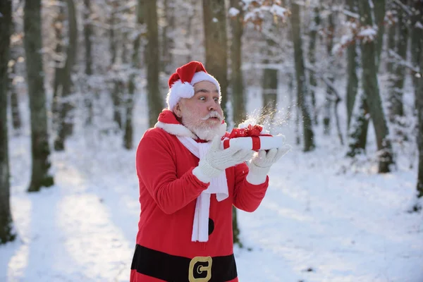 Funny Santa souffler de la neige sur le cadeau de Noël, à l'extérieur. — Photo