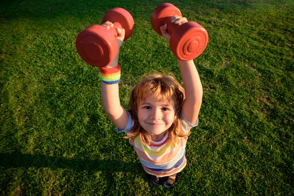 Stark liten pojke. Lustigt barn med hantlar. Barnens hälsa. Utanför. Kondition och energi. Barndomsverksamhet. Gym träning. Sportig pojke är kul. Spännande liten idrottsman. Framgång. — Stockfoto