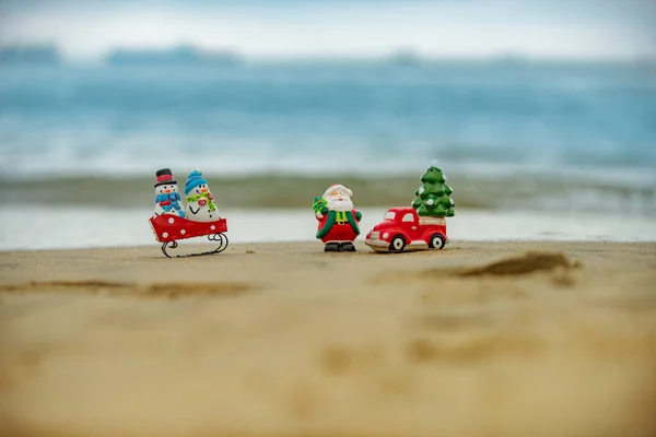 Świąteczne tło. Zabawka Santa i bałwan na plaży letniej, koncepcja podróży w gorących krajach. — Zdjęcie stockowe