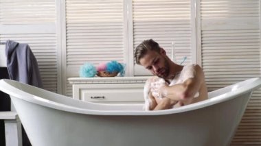 Banyoda tıraş makinesi olan kendine güvenen bir adam. Banyo konsepti. Küvette banyo yapan genç bir adam. Gay konsepti. Erkek güzelliği, bakımlı vücut ve cilt konsepti.