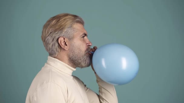 Balon patlaması. Hava balonunun üzerinde iğne tutan komik bir adam, bir an balonu patladı. Mavide izole edilmiş. Balonu iğneyle delen çılgın adam.. — Stok video