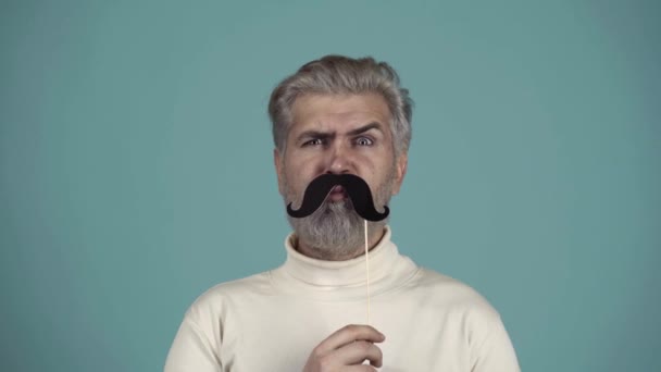 En man med pappersmustasch. Skägg rolig hipster. Ansikte på människan med olika känslor. Spännande kille, mänskliga känslor, ansiktsuttryck. Man skäggig hipster med svart mustasch. — Stockvideo