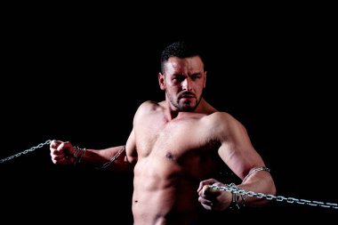 Çıplak gövdeli genç bir sporcu. Zincirli, üstsüz, vahşi bir adamın yakın plan portresi. Siyah arka plandaki atlet..