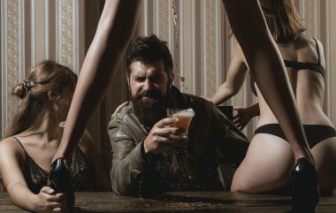Masada duran güzel uzun bacaklı seksi seksi kadın ve meyhanede sakallı yakışıklı adam için bira çiziyor. Sakallı adam bira içiyor ve etrafında seksi kadınlar var..