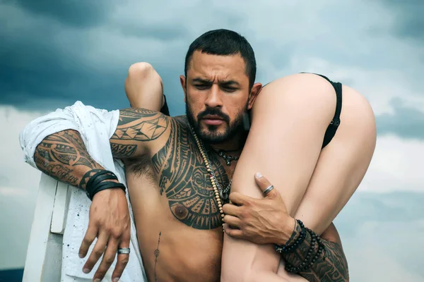 Man holding woman with sexy hot ass. Strong muscular tattooed bearded man holding his sexy fit woman with hot butt isolated at grey background. Eternal love and trust concept. —  Fotos de Stock