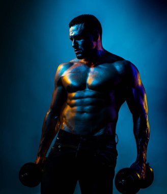 Gömleksiz seksi vücut geliştirici halterle egzersiz yapıyor. Neon mavi ışık.