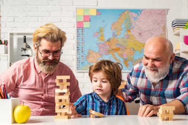 Fotoğrafta gülümseyen büyükbaba, baba ve anaokulu çocuğu kameraya bakıyor. Evde Jenga oyunu.
