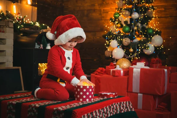 Glückliches Kind mit Weihnachtsgeschenkschachtel. Weihnachtsdekoration. Glückliches Kind öffnet Weihnachtsgeschenkbox. Lustiges Baby mit Nikolausmütze. LED-Licht. — Stockfoto