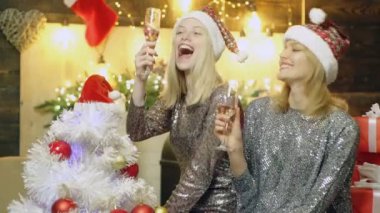 Noel şapkalı, şampanya kadehleriyle kadeh kaldıran iki mutlu kız. Noel Baba şapkasını paylaşan tatlı bir kadın. Yeni Yıl.
