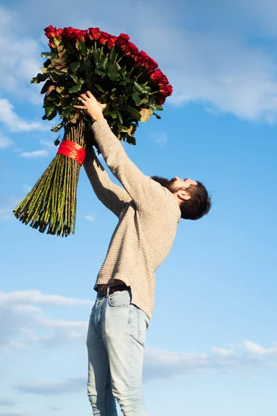 Hombre con un gran ramo de rosas. Celebra el Día de San Valentín y Regalos Románticos. Un tipo guapo sostiene un ramo de rosas rojas grandes. Hombre guapo dando flores a su amante en el Día de San Valentín. — Foto de Stock