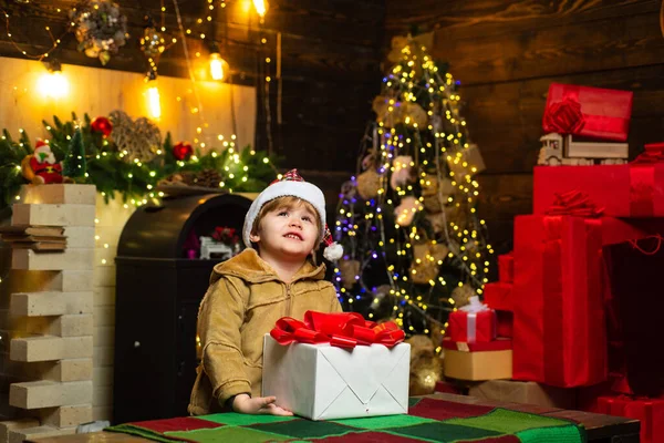 Świąteczne dziecko chce wiedzieć, co jest w pudełku świątecznym. Szczęśliwy mały uśmiechnięty chłopiec z pudełkiem świątecznym. Koncepcja wakacji. Ciekawski.. — Zdjęcie stockowe