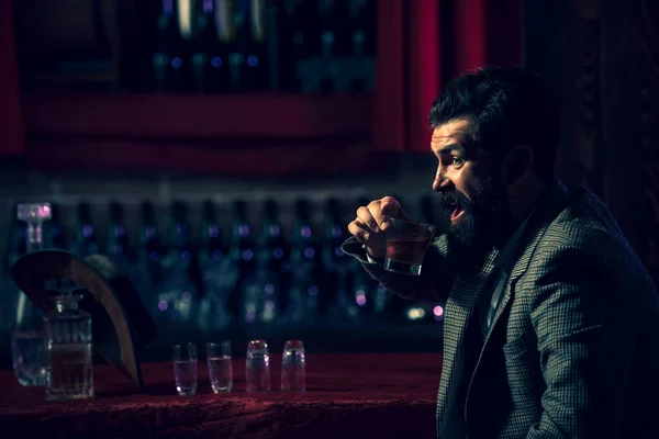 Hipster macho con barba elegante beber coñac, vodka o brandy sentado en el bar. — Foto de Stock