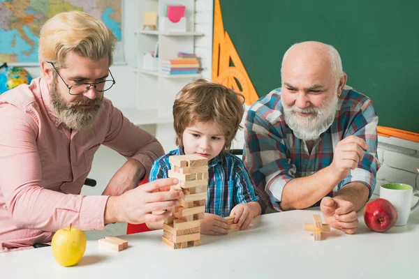 祖父は息子と孫が家庭でボードゲームをしているのを見ている。家族向けゲーム. — ストック写真