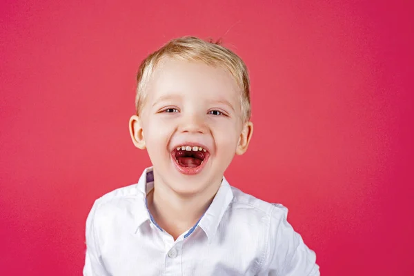 Lustige Kindergesichter. Kind, das Überraschung und Glück ausdrückt. Porträt eines lächelnden Jungen isoliert mit blauen Augen isoliert auf rot. — Stockfoto