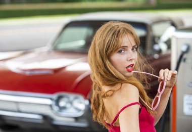 Benzin istasyonunda kırmızı elbiseli genç bir kadın. Benzin istasyonunda çekici, zarif bir kız yakıt ikmali yapıyor..