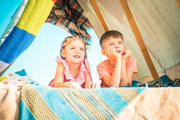 As crianças relaxam no acampamento. Família feliz amar crianças irmão e irmã jogar na tenda escura na natureza. — Fotografia de Stock