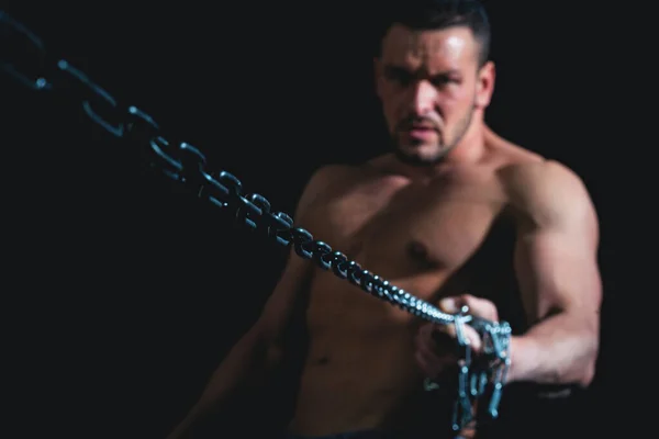 Guy på svart med ansträngda muskler håller en rostig metall kedja, ett begrepp av styrka man makt. — Stockfoto