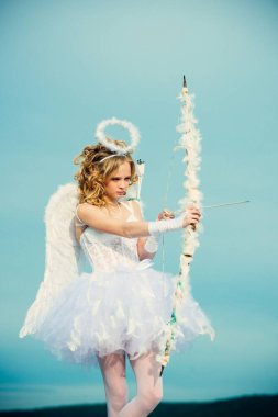 Aşk tanrısı kızı aşk okuyla birini hedef alıyor. Aşkın oku. Güzellik gözlerini maviye boyadı. Güneş ışığında büyüleyici bir kadın. Beyaz kanatlı melek çocuk kız. Sevgililer Günün kutlu olsun.