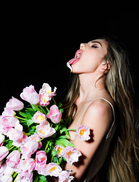 Sensueel meisje met bloemen boeket geïsoleerd op zwart. Jonge mooie vrouw met boeket van roze tulpen over geïsoleerde achtergrond steken tong uit, grappige uitdrukking. Emotieconcept. — Stockfoto