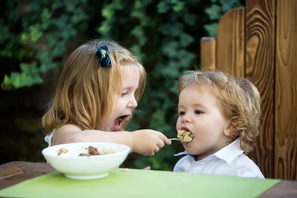 Sister feeding baby boy. Girl feeds brother with a spoon. Kid food. — Stock Photo, Image