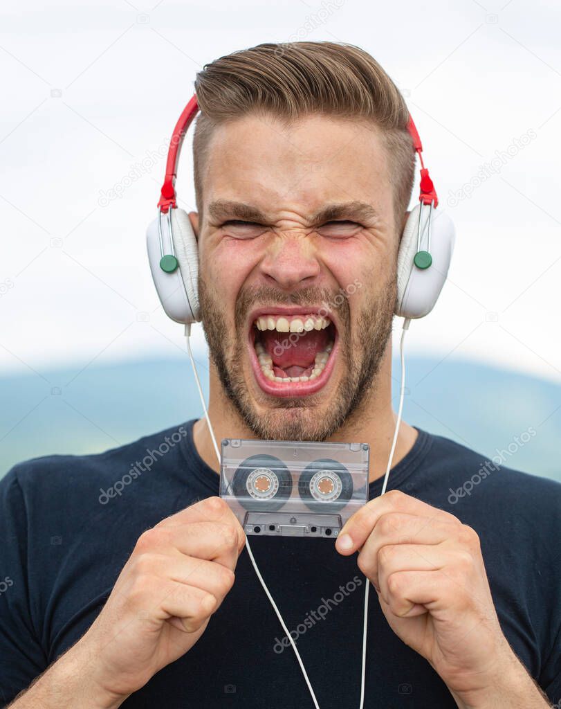 Excited Man listening music in headphones with cassette. Emotional screaming portrait guy. Young bearded good-looking casual man with and earphones in the style of the 90s, with retro cassetteplayer.