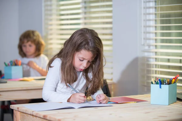 Retrato de menina bonito sentado na mesa em sala de aula da escola. Desenho de aluno, estudo de criança pré-escolar na escola. Educação infantil, conceito de ensino em casa. — Fotografia de Stock