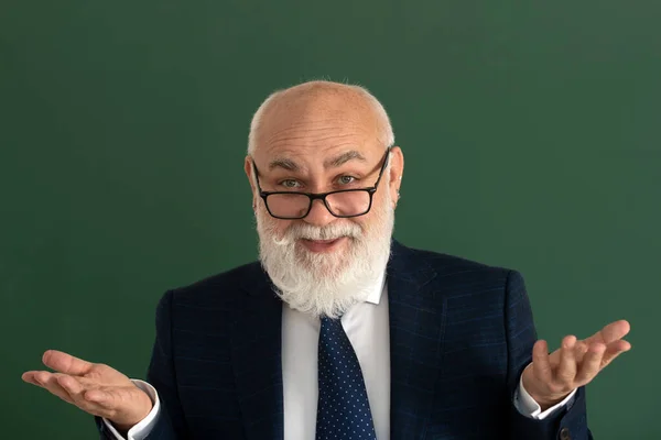 Alter Lehrer mit offenen Armen im Klassenzimmer. Fröhlich freundliche Seniorin vor einer Tafel. Lustiger Professor oder Wissenschaftler im eleganten Anzug. — Stockfoto