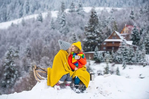 Merry Christmas and Happy new year. Happy winter children kissed. Kids Romantic Picnic. Little couple sitting on sled hugging and kissing. Children friends kiss in snow. love story. — Stock Photo, Image