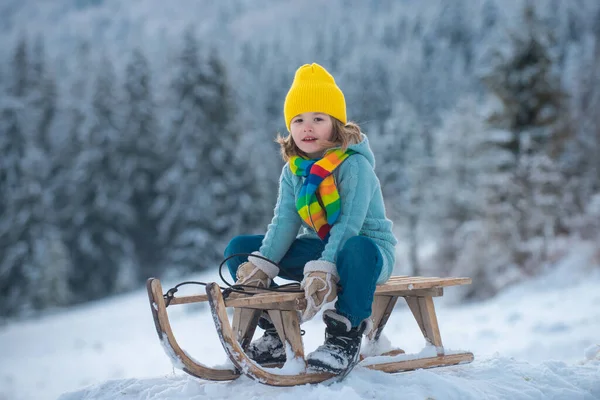 Les enfants d'hiver. Enfant garçon glissant sur un traîneau dans un parc enneigé. Petit garçon jouant dehors dans la neige. — Photo