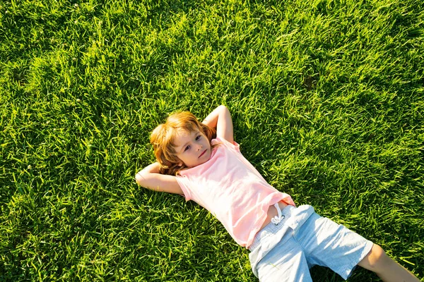 Joli gosse allongé sur fond d'herbe. Joyeux garçon insouciant jouissant sur le terrain et rêvant. Unité avec la nature. — Photo