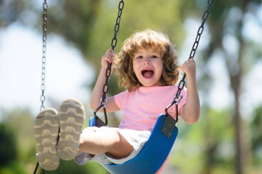 Arka bahçede çocuk salıncağı. Çocuk dışarıda oynuyor. Mutlu küçük çocuk sallanıyor ve sağlıklı yaz tatili aktiviteleri yapıyor..